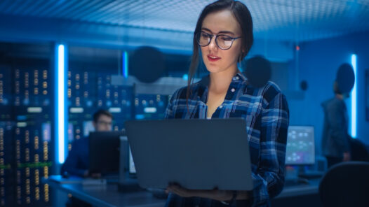 A smart young woman selects fraud management solutions on a laptop with server racks in the background.