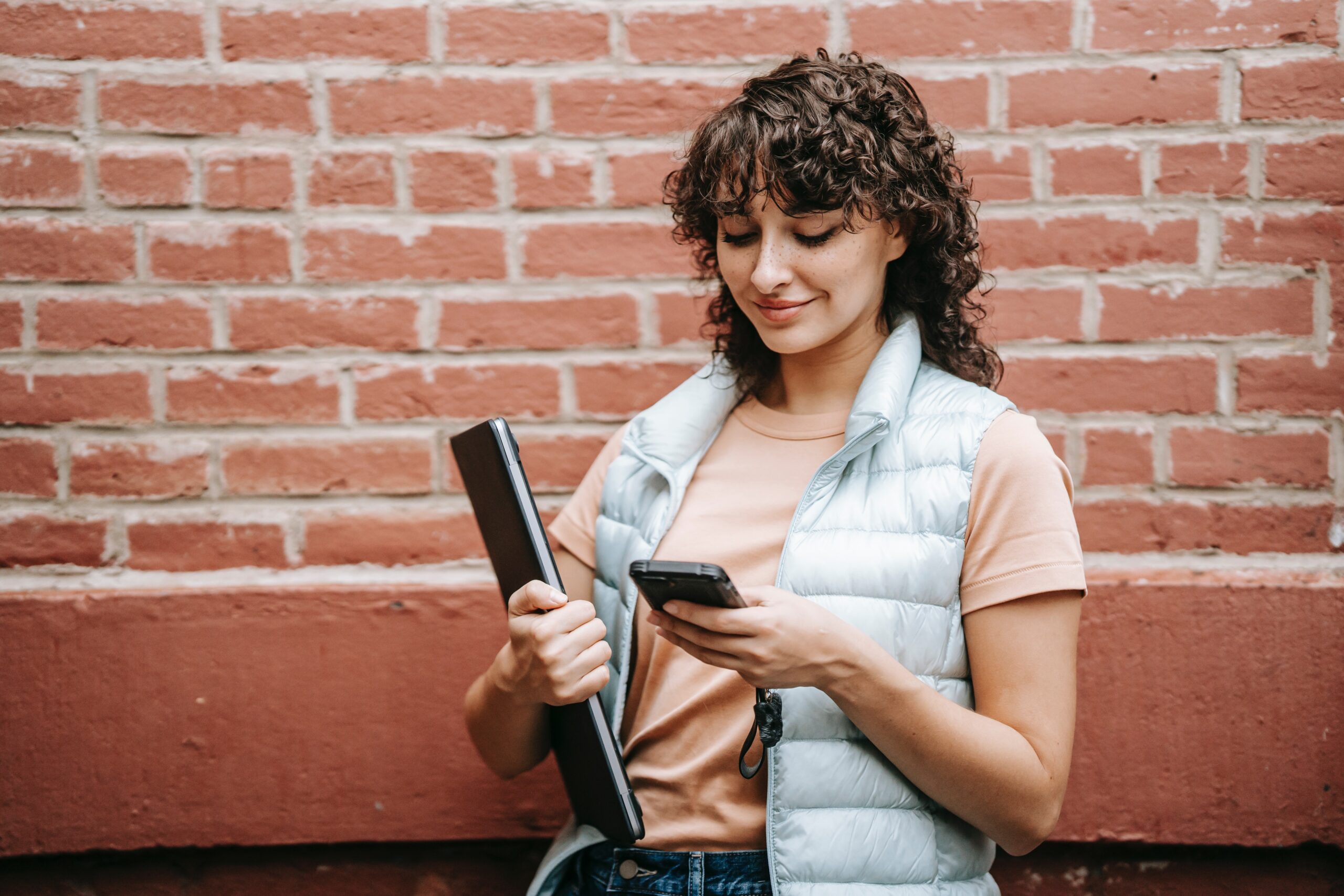 woman holds laptop and looks at mobile phone