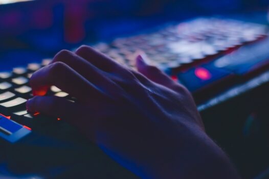 A man types on a backlit keyboard in the dark